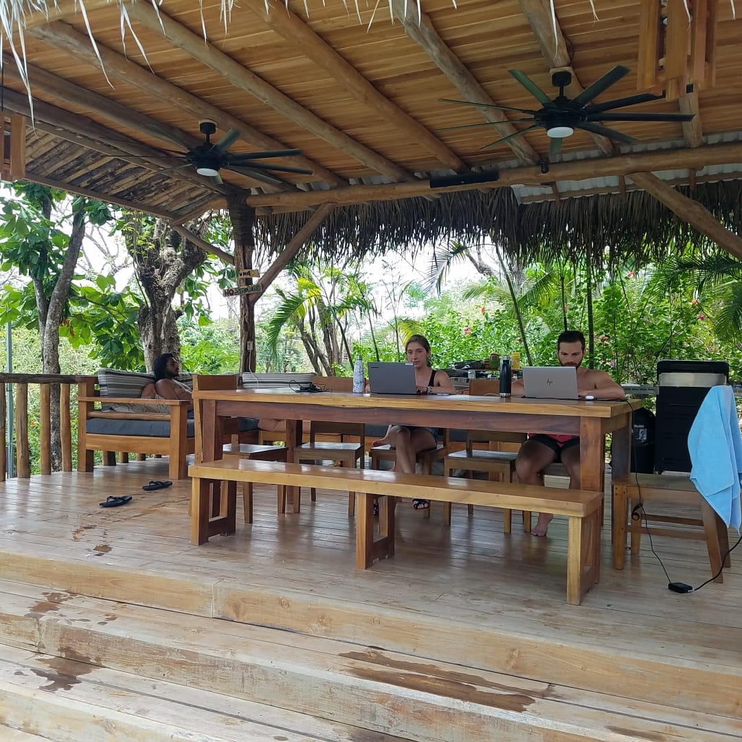 Guests working side by side under the thatched rancho with ceiling fans.