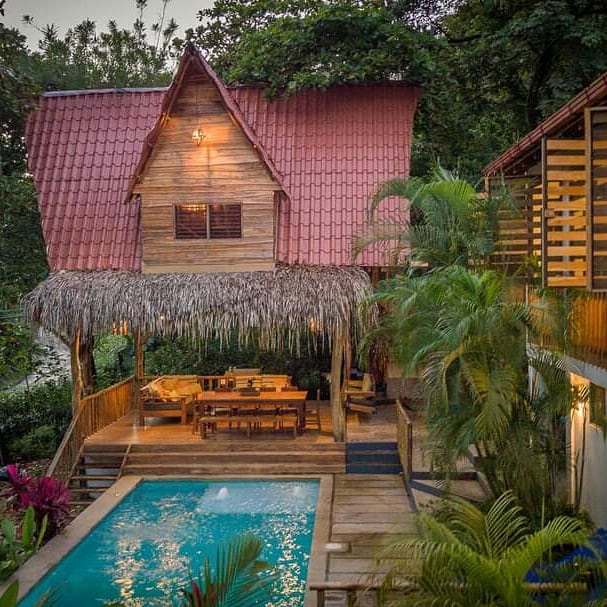 Casa Brisa side after — thatched rancho and clay-tile treehouse addition above the pool with a long wooden dining table under the roof.