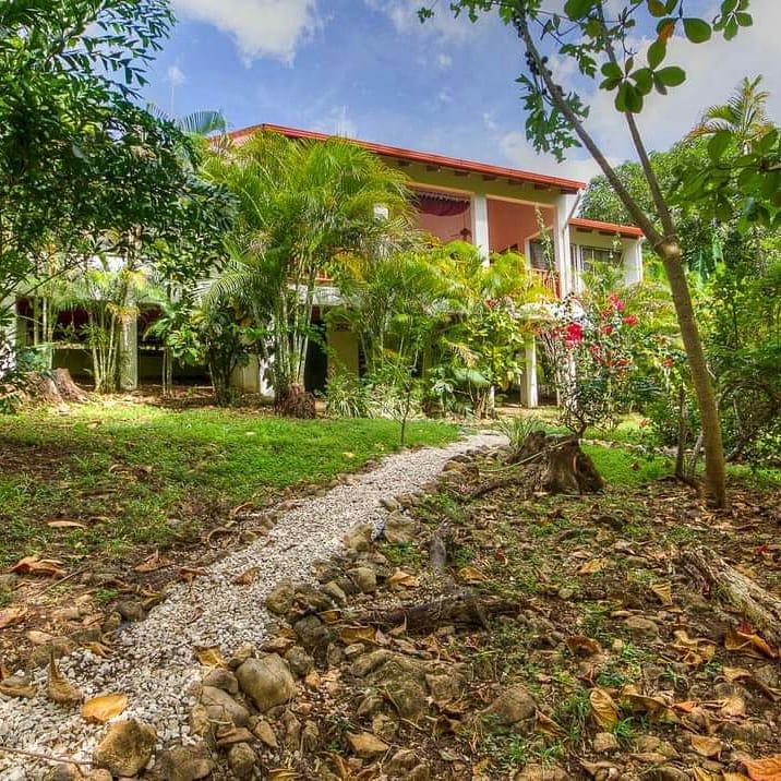 Casa Brisa before renovation — a peach-colored two-story villa with a red concrete roof behind an overgrown garden and a rock-lined path.