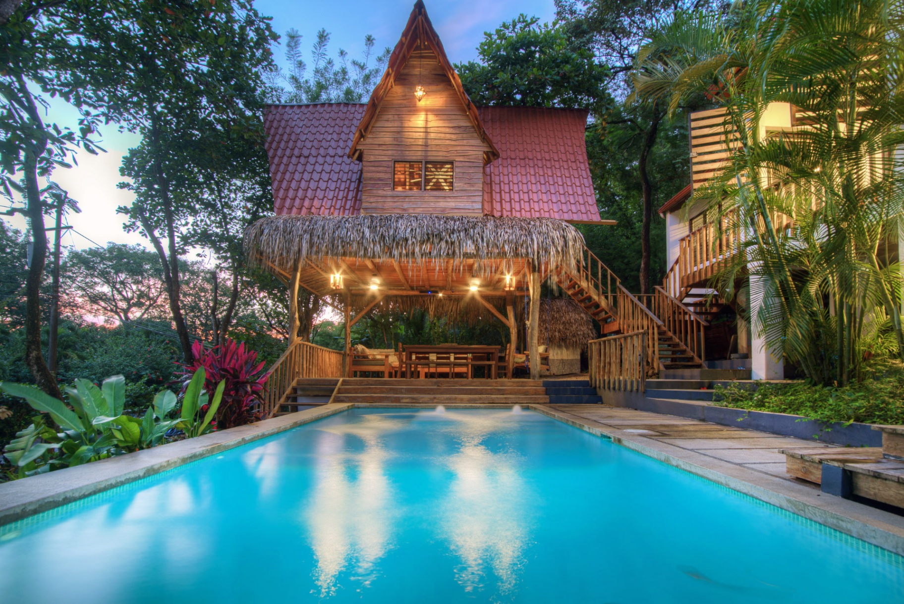 Open-air rancho with hanging swing bench, dining table, lounge seating and saltwater pool