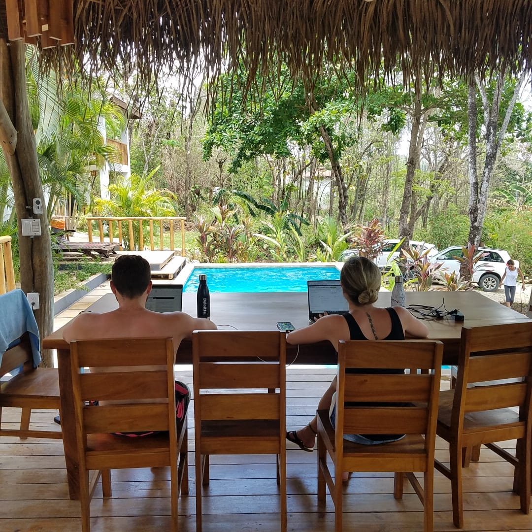 Two guests working on laptops at the rancho table overlooking the pool.