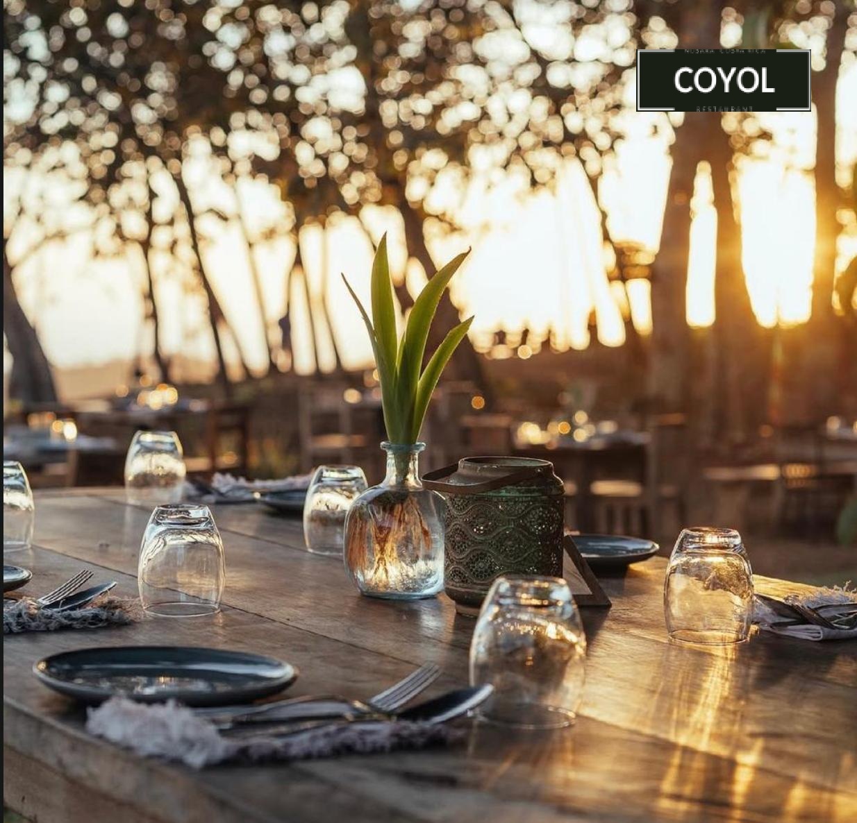 Candle-lit wooden table under the trees at Coyol restaurant in Nosara at golden hour.
