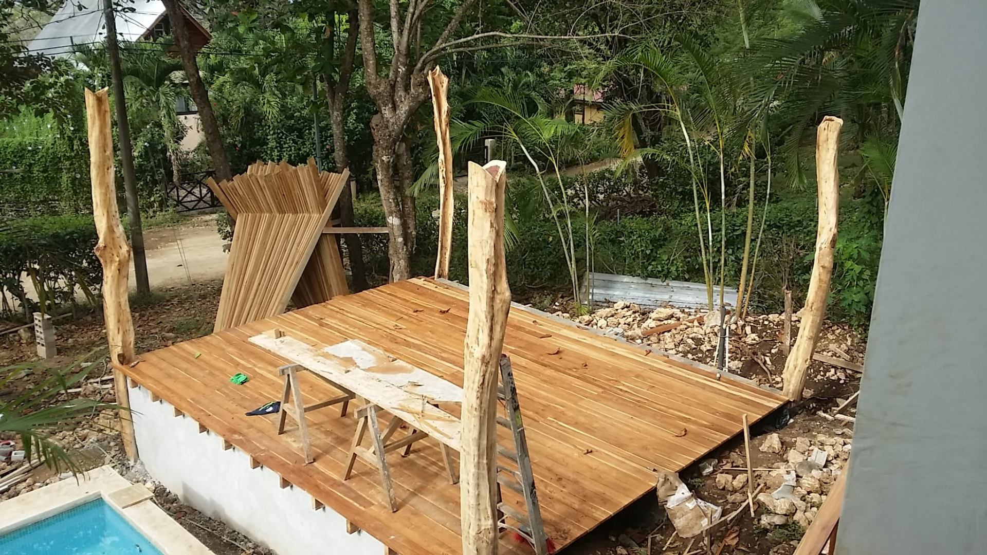Fresh wooden deck of the rancho with peeled round-timber posts being set into place beside the pool.