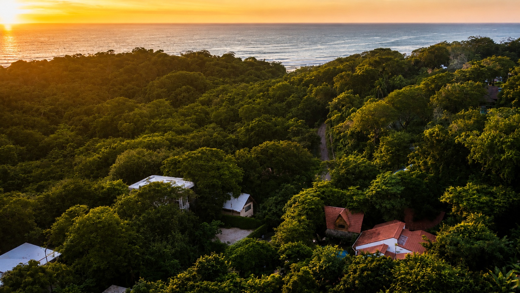 Golden-hour aerial looking west from Hacienda Nosara over the Playa Pelada jungle canopy to the Pacific Ocean.